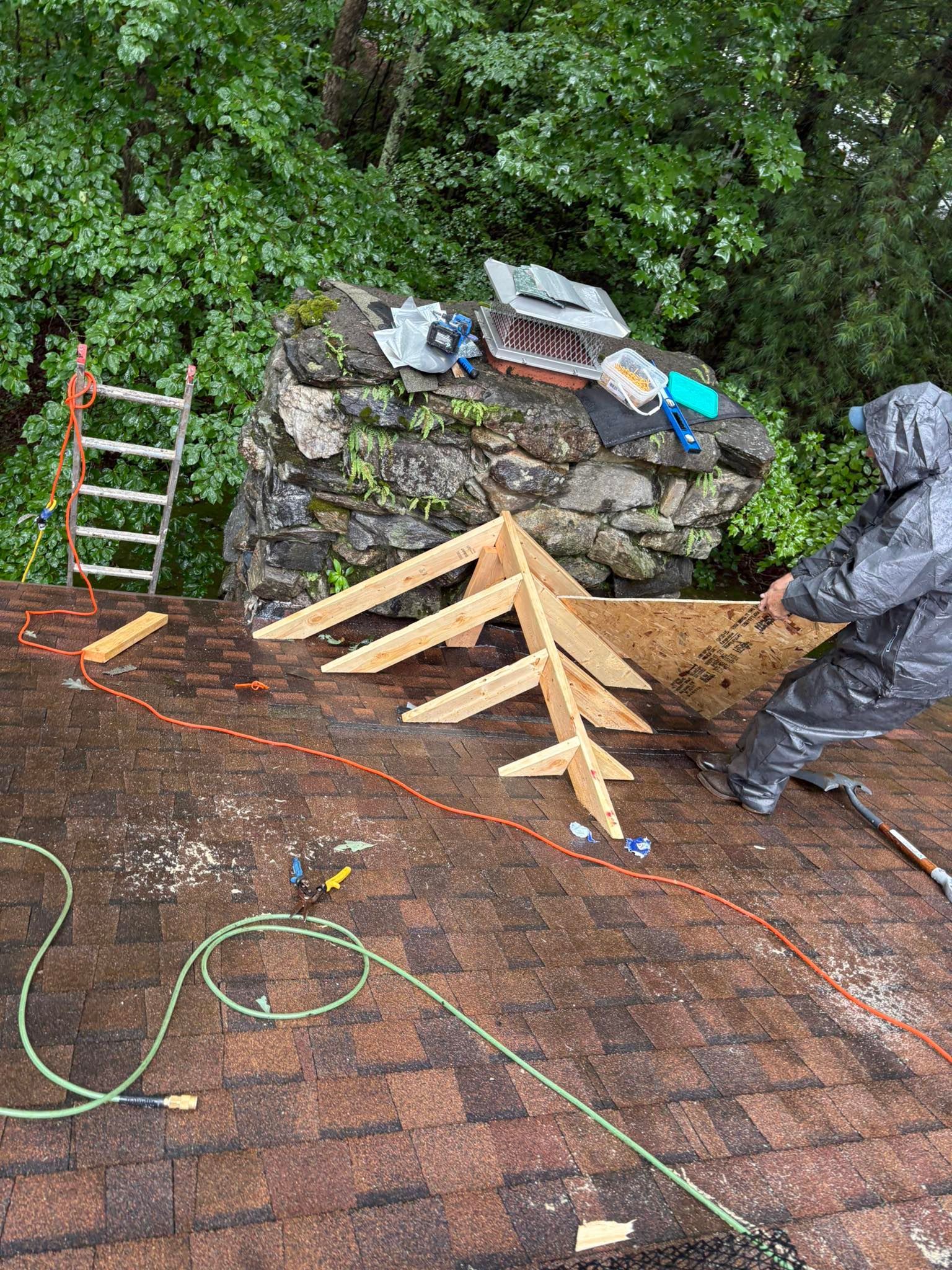 A person on a roof in the rain is working on a frame, near a chimney.