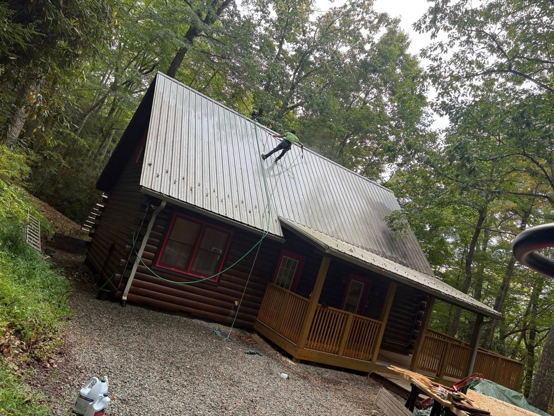 Person on a roof of a brown cabin surrounded by trees.
