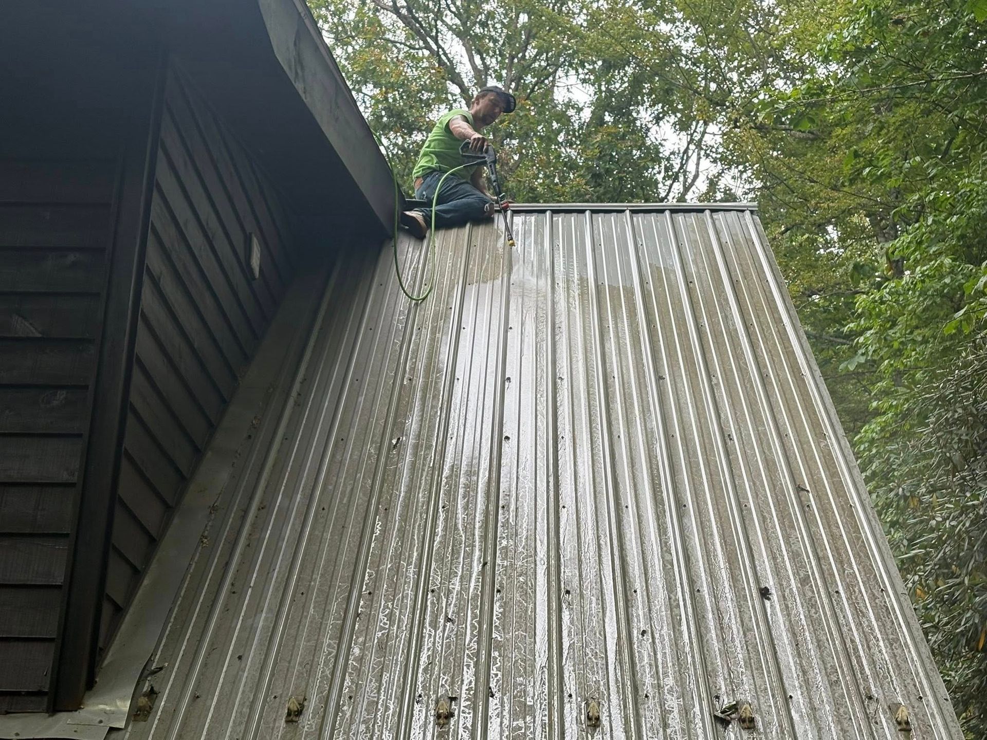 Man power washing a metal roof of a building in an outdoor setting.