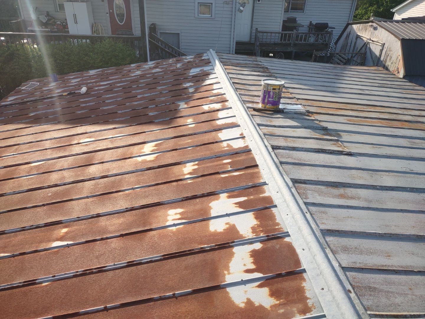 Rusty metal roof being painted, with partial coverage; paint can visible.