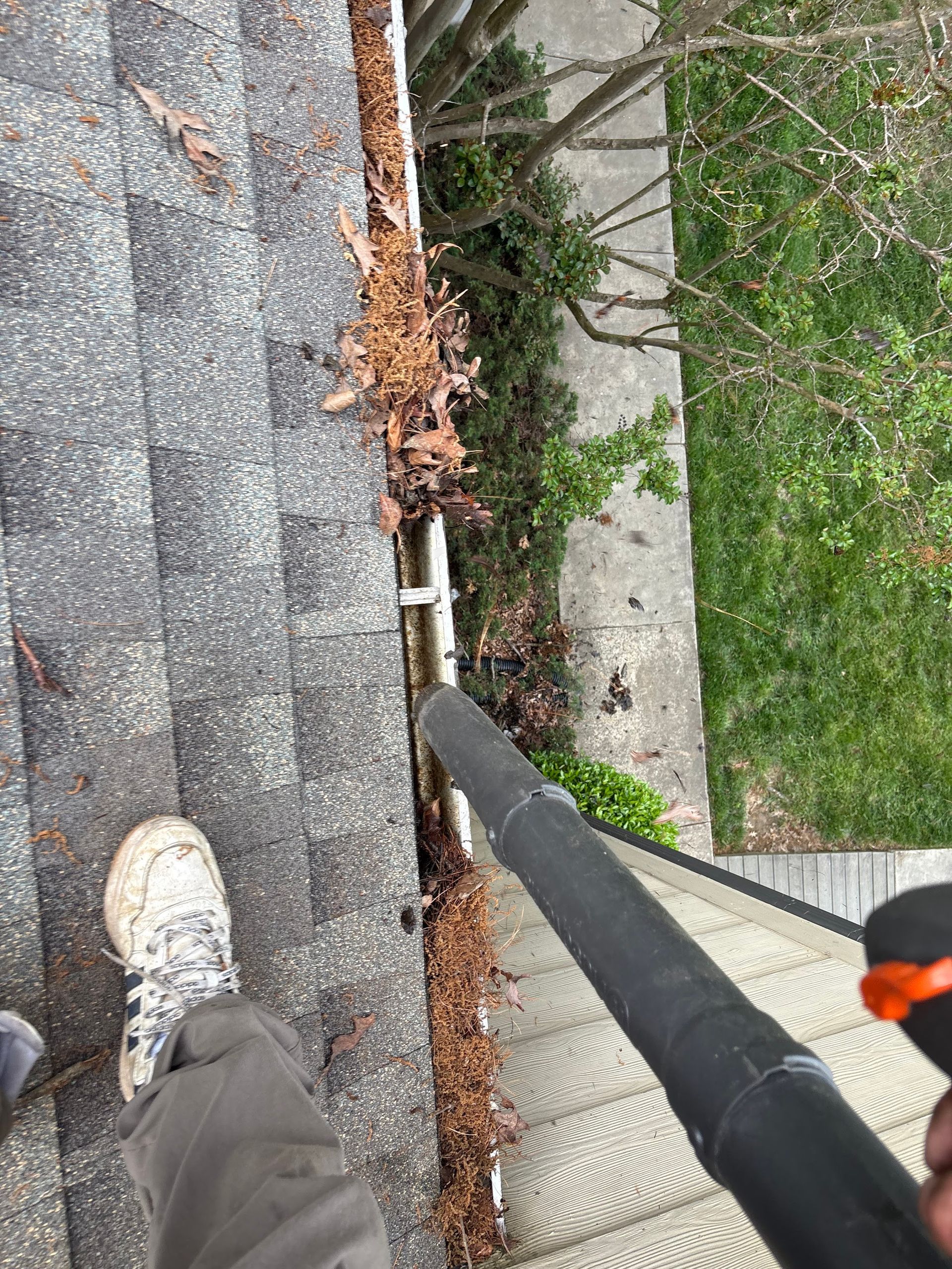 Person using a leaf blower to clean debris from a roof gutter.