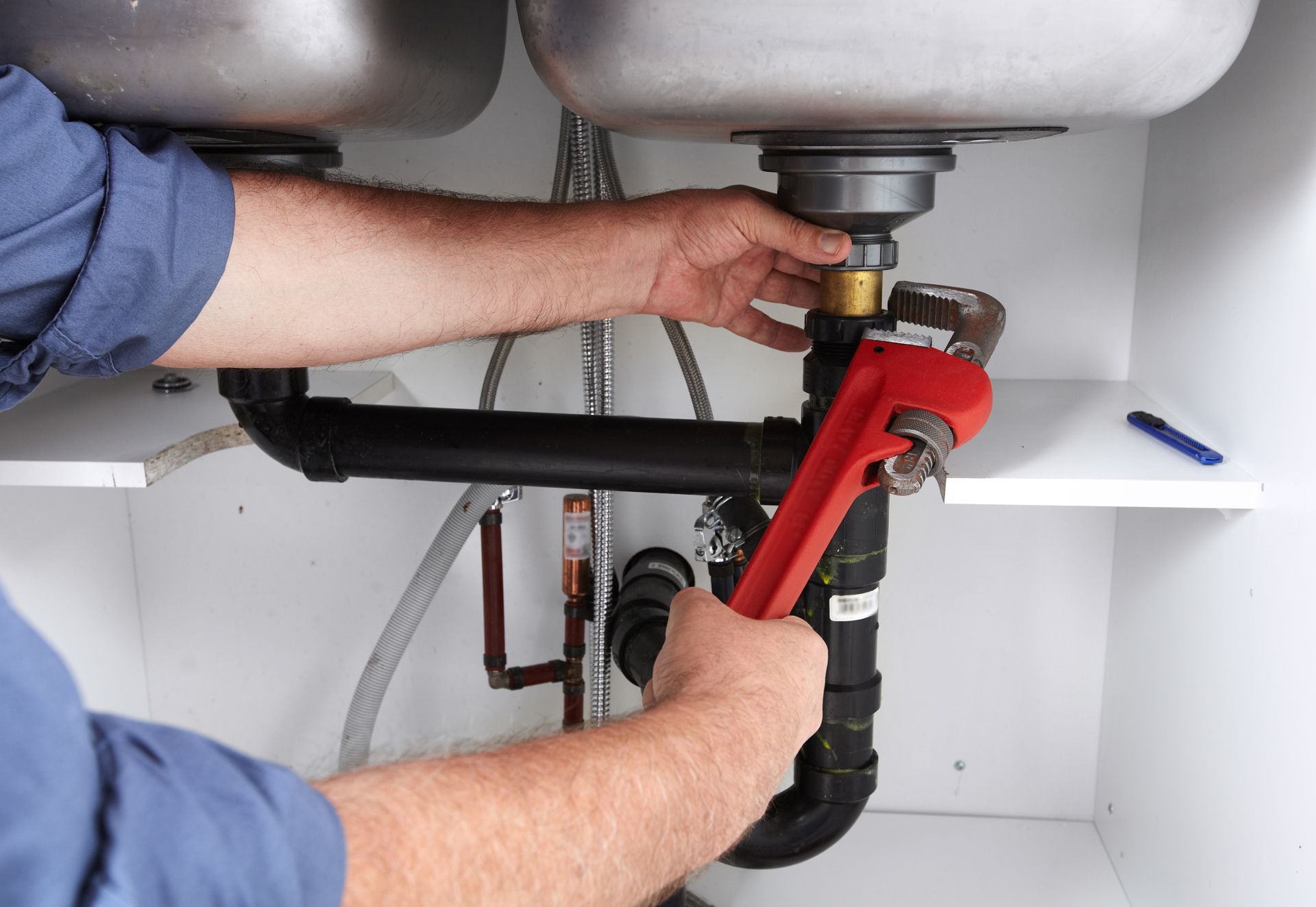 Person using a wrench to work on pipes under a kitchen sink.