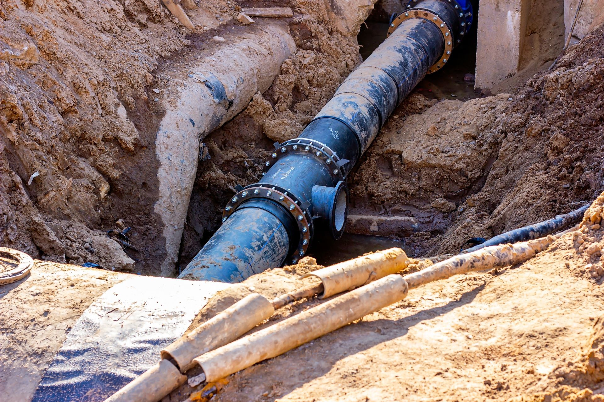 A buried water pipe in an excavated ditch, with a blue valve and connecting pipes visible.
