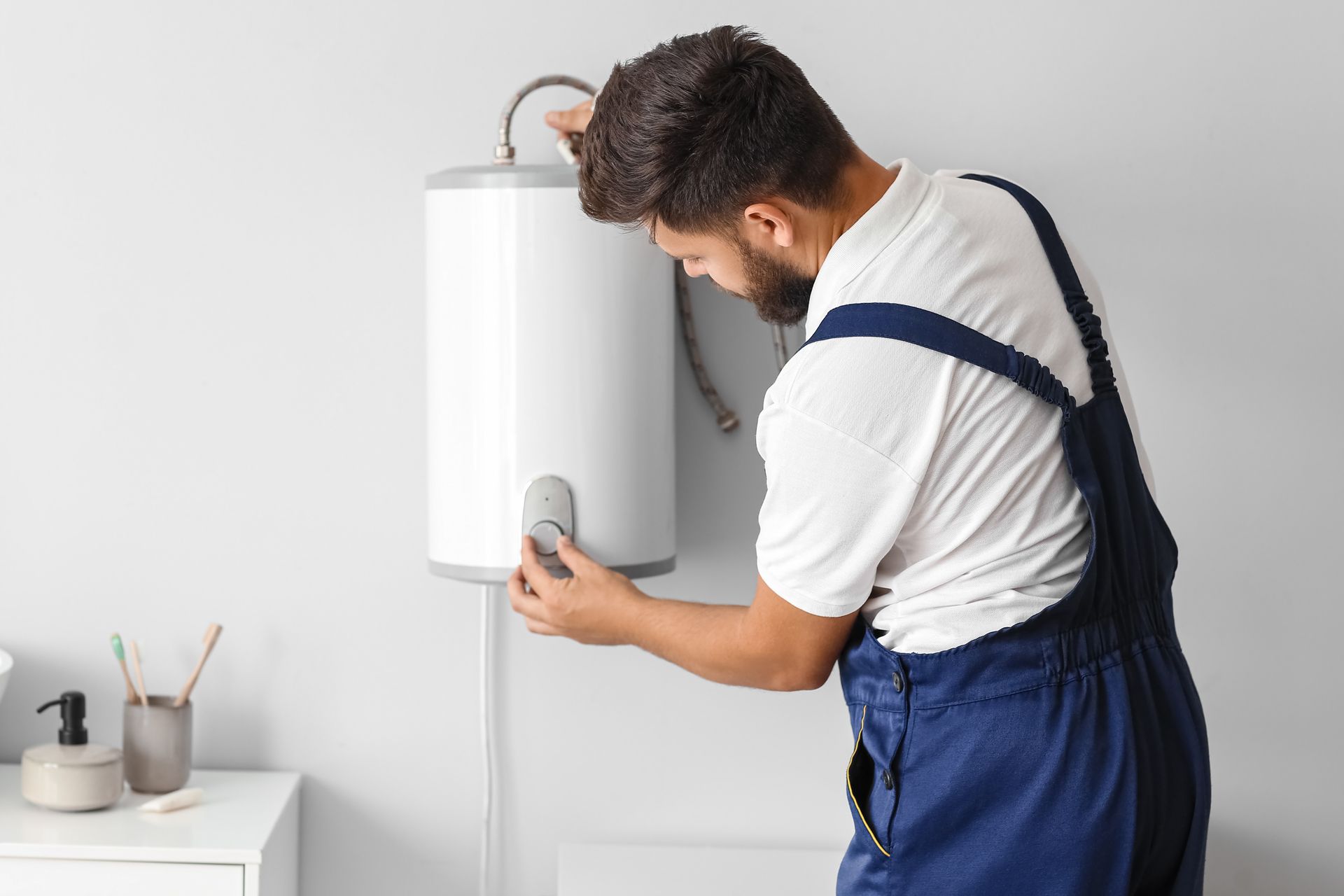 Person in red shirt and overalls adjusts a white wall-mounted heater.