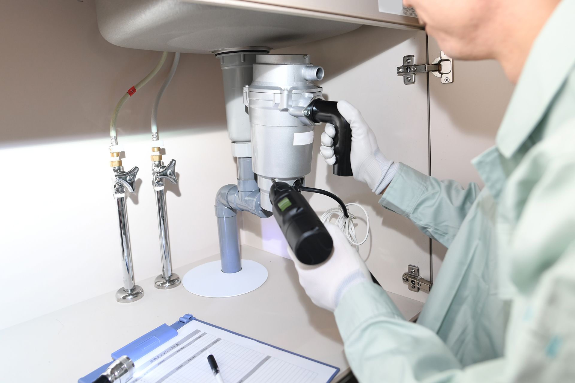 Plumber inspecting a kitchen sink with a garbage disposal and tools.