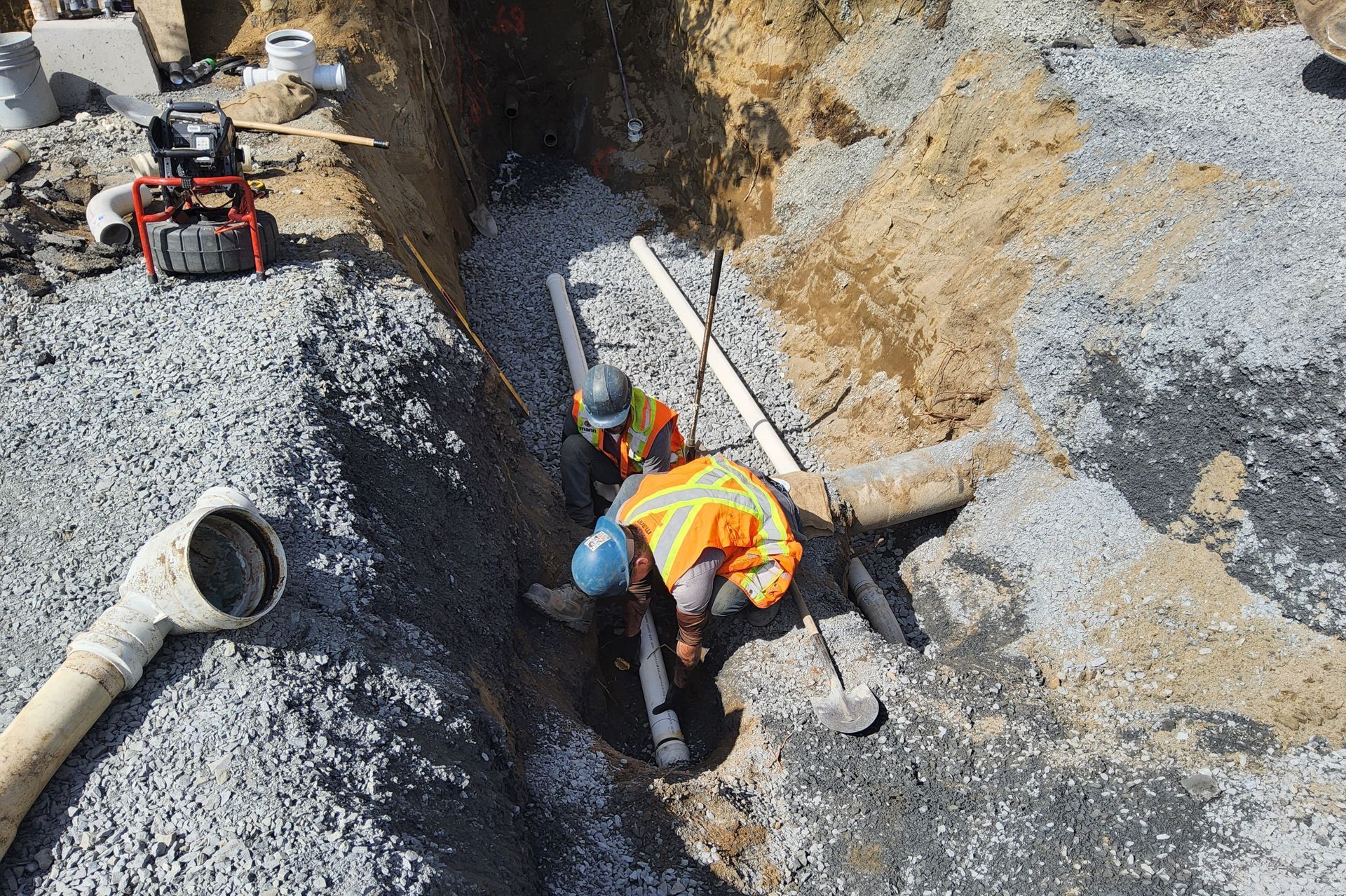 Two construction workers installing pipes in a gravel-lined trench.
