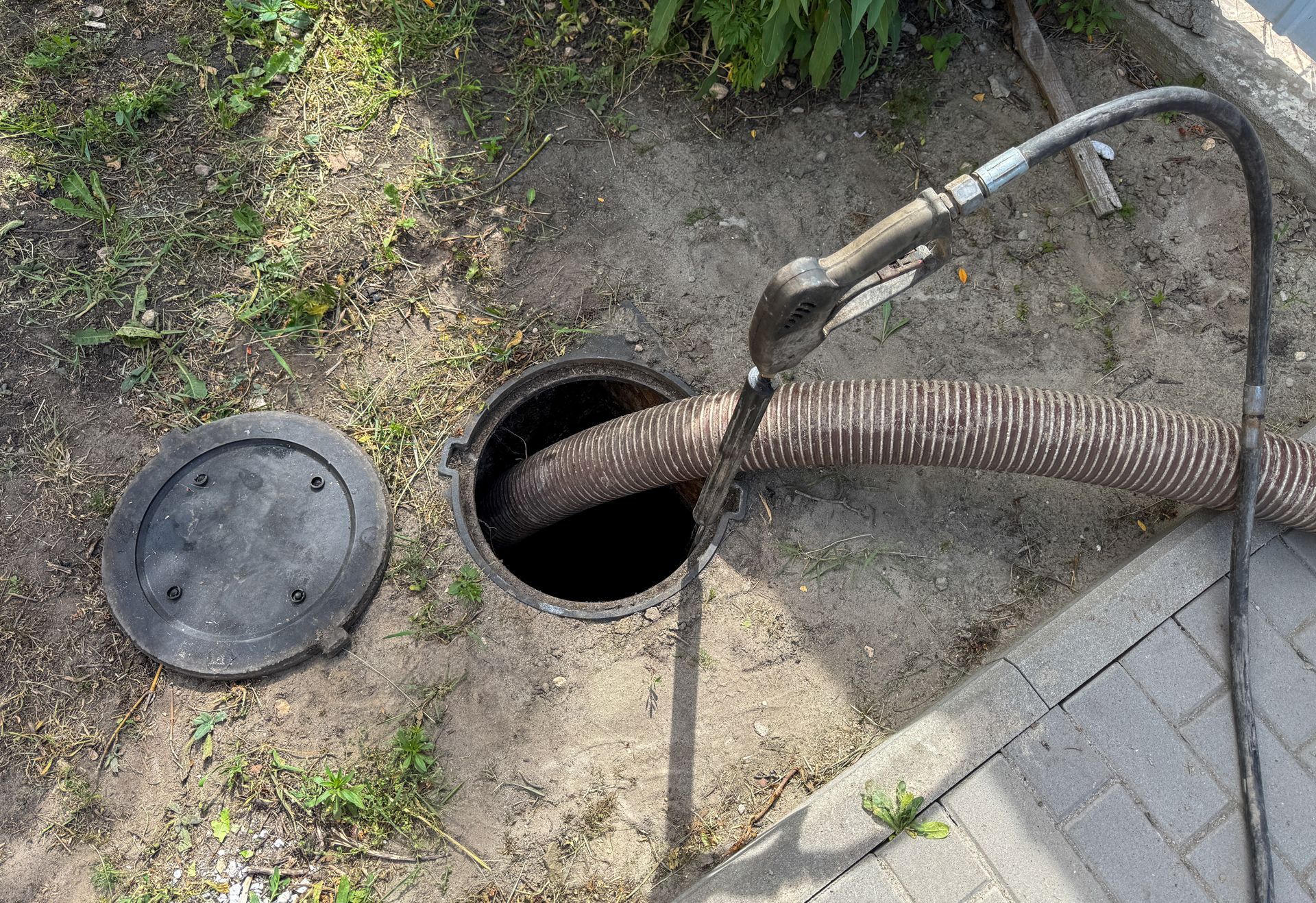 Open septic tank with hose inserted, lid nearby, outdoors.