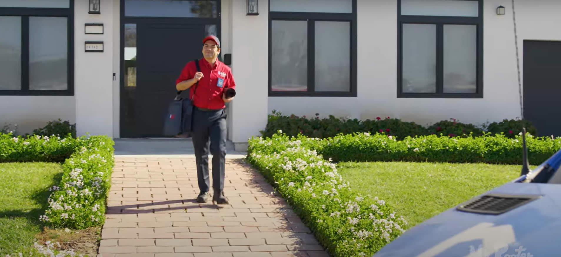 A professional wearing a red uniform and cap shows a tablet screen to a person while standing in a home.