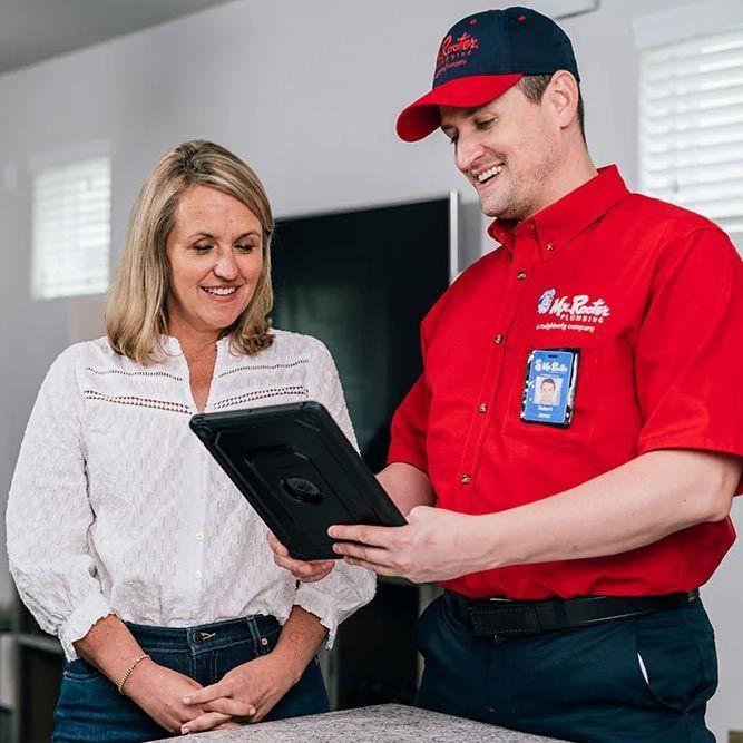 A professional wearing a red uniform and cap shows a tablet screen to a person while standing in a home.