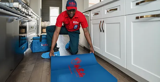 A professional wearing a red uniform and cap shows a tablet screen to a person while standing in a home.