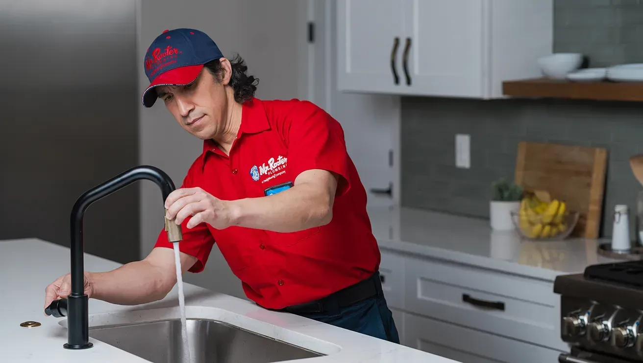 A professional wearing a red uniform and cap shows a tablet screen to a person while standing in a home.