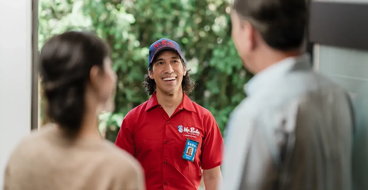 A professional wearing a red uniform and cap shows a tablet screen to a person while standing in a home.