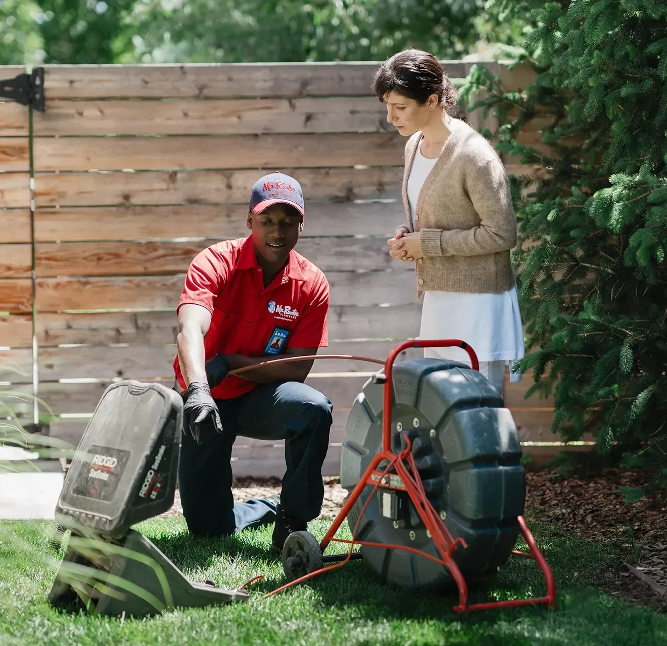 A professional wearing a red uniform and cap shows a tablet screen to a person while standing in a home.