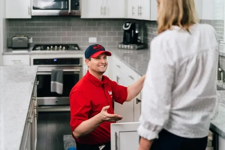A professional wearing a red uniform and cap shows a tablet screen to a person while standing in a home.