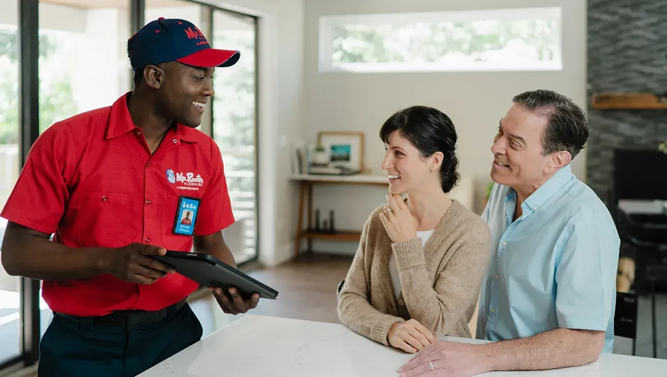 A professional wearing a red uniform and cap shows a tablet screen to a person while standing in a home.