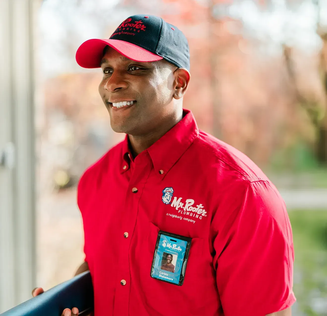 A professional wearing a red uniform and cap shows a tablet screen to a person while standing in a home.