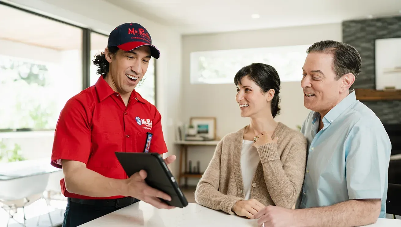 A professional wearing a red uniform and cap shows a tablet screen to a person while standing in a home.