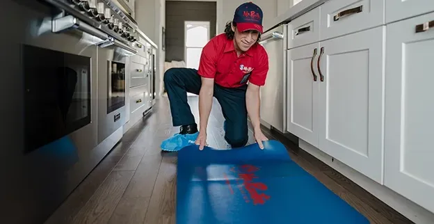 A professional wearing a red uniform and cap shows a tablet screen to a person while standing in a home.