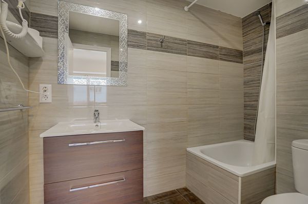 Baño moderno de color beige con tocador, espejo y zona de ducha con bañera.