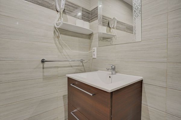 Lavabo moderno con mueble de madera, paredes alicatadas en color beige, espejo y toallero.
