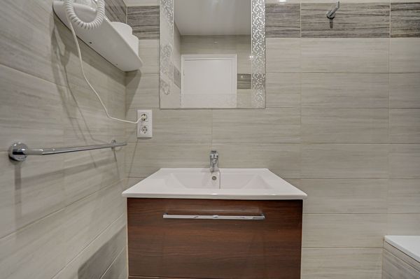 Baño moderno con paredes alicatadas, tocador de madera, lavabo blanco, espejo, toallero y grifería de ducha.