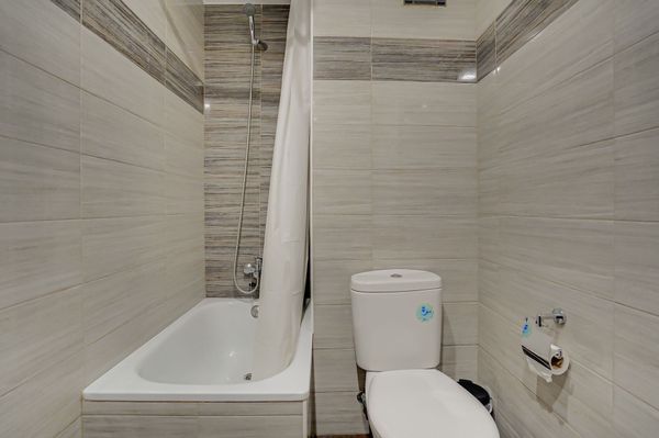 Baño moderno con azulejos beige, bañera, inodoro y cortina de ducha.