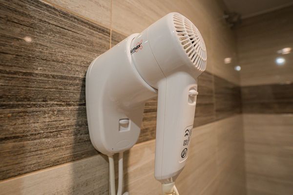 Secador de pelo blanco montado en la pared en un baño con azulejos que imitan madera.