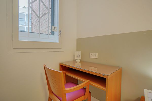 Un pequeño escritorio con una silla naranja junto a una ventana en una habitación de colores claros.