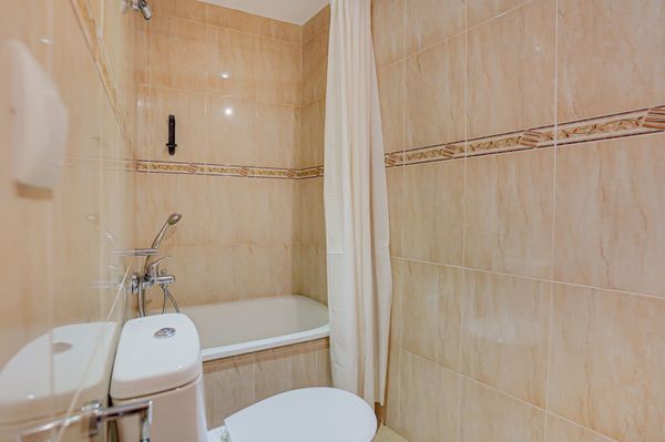 Baño pequeño con azulejos beige, bañera, inodoro, lavabo y cortina de ducha.