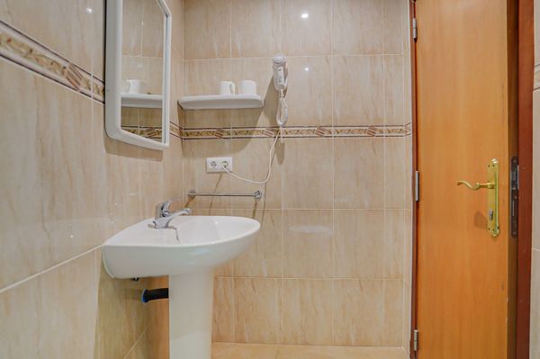 Pequeño baño de color beige con lavabo de pedestal blanco y puerta de madera.