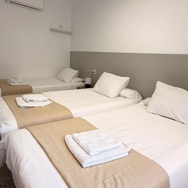 Dos camas individuales en habitación minimalista blanca con colchas beige y toallas dobladas.
