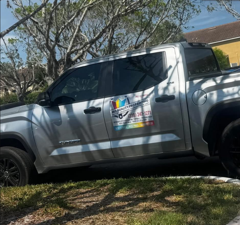 A silver crew-cab pickup truck parked on grass, featuring a colorful business logo on the driver-side door.