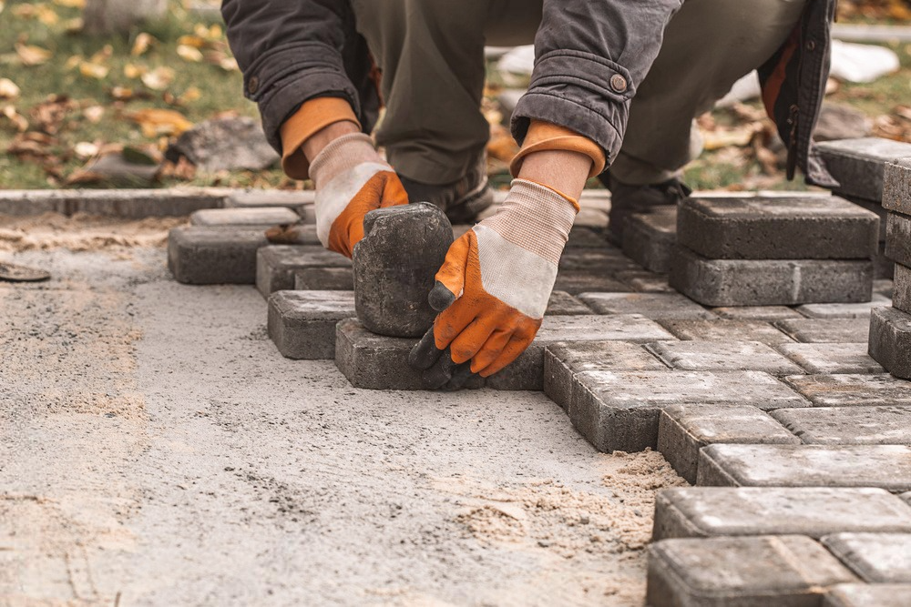 a man is laying bricks on a sidewalk .