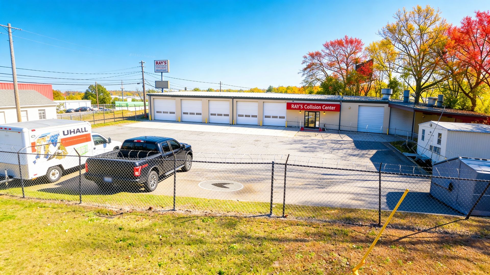 A commercial building with garage doors, a U-Haul truck, and a pickup truck on a sunny day.