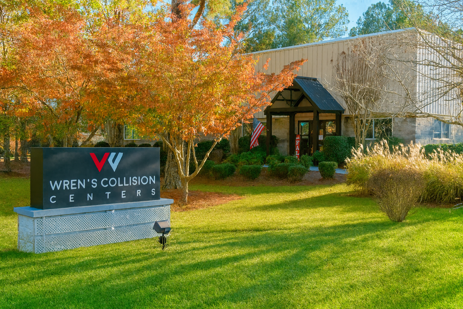 Wren's Collision Center building with sign and autumn foliage, sunny day.