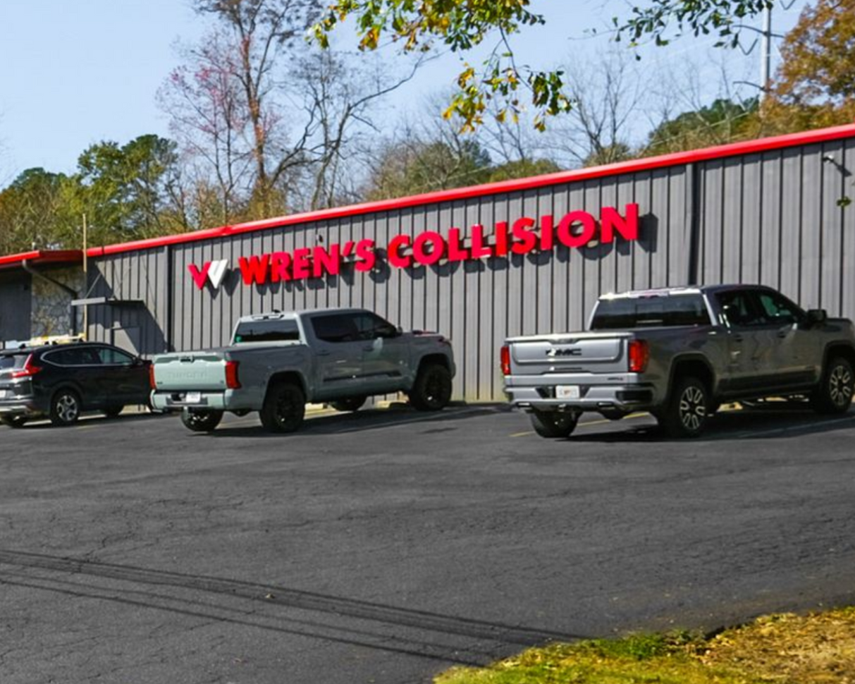 Wren's Collision building with a red sign, gray exterior, and multiple trucks parked out front.