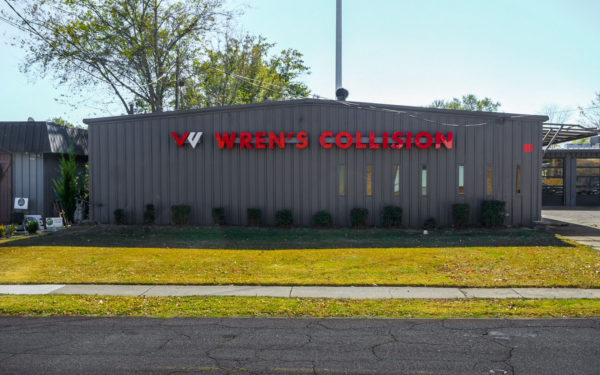 Wren's Collision auto body shop with red signage on gray building; green grass and trees in background.