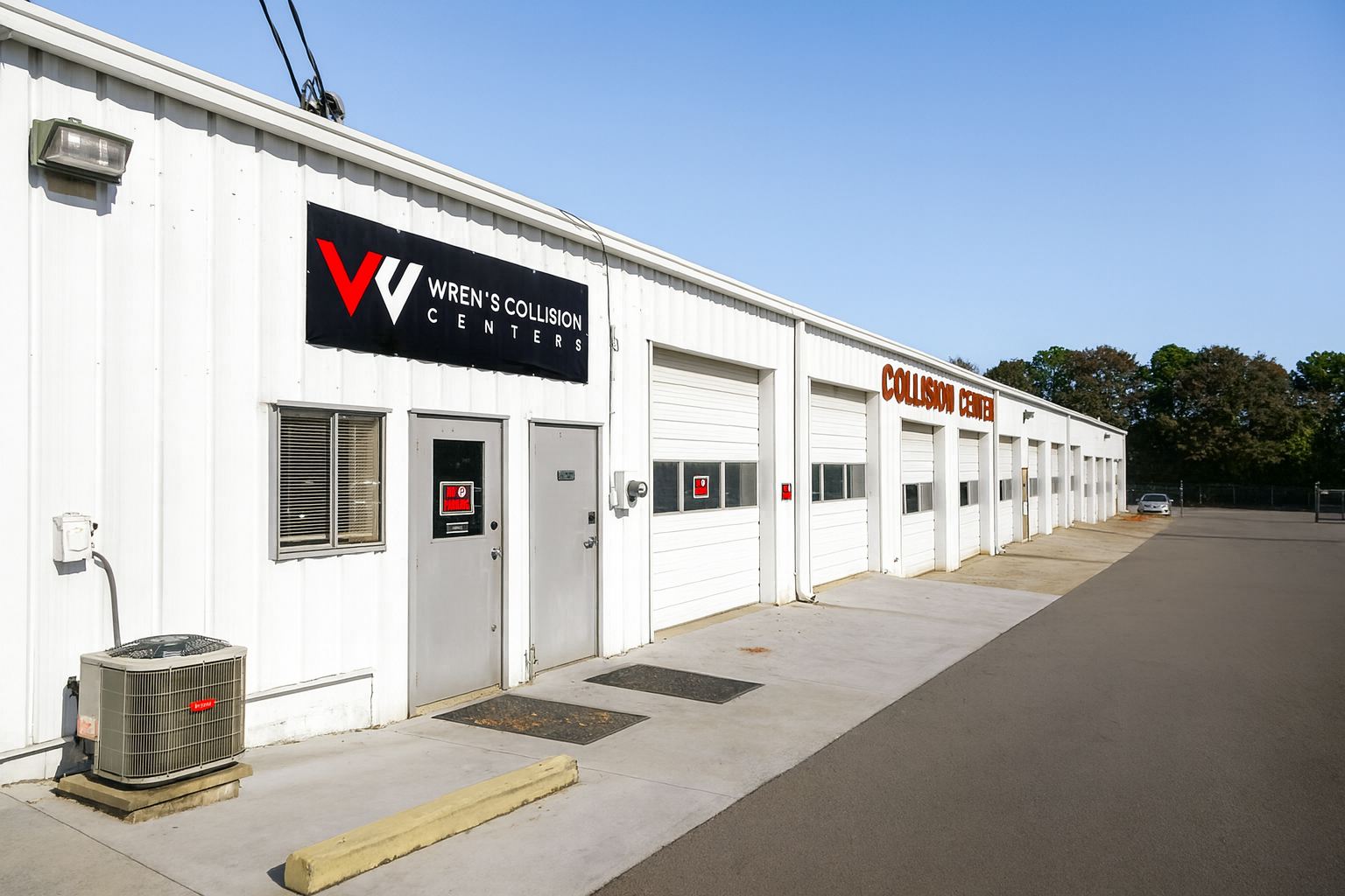 White industrial building with roll-up doors, signage for VINCENT'S COLLISION CENTER. Exterior with paved area and a blue sky.