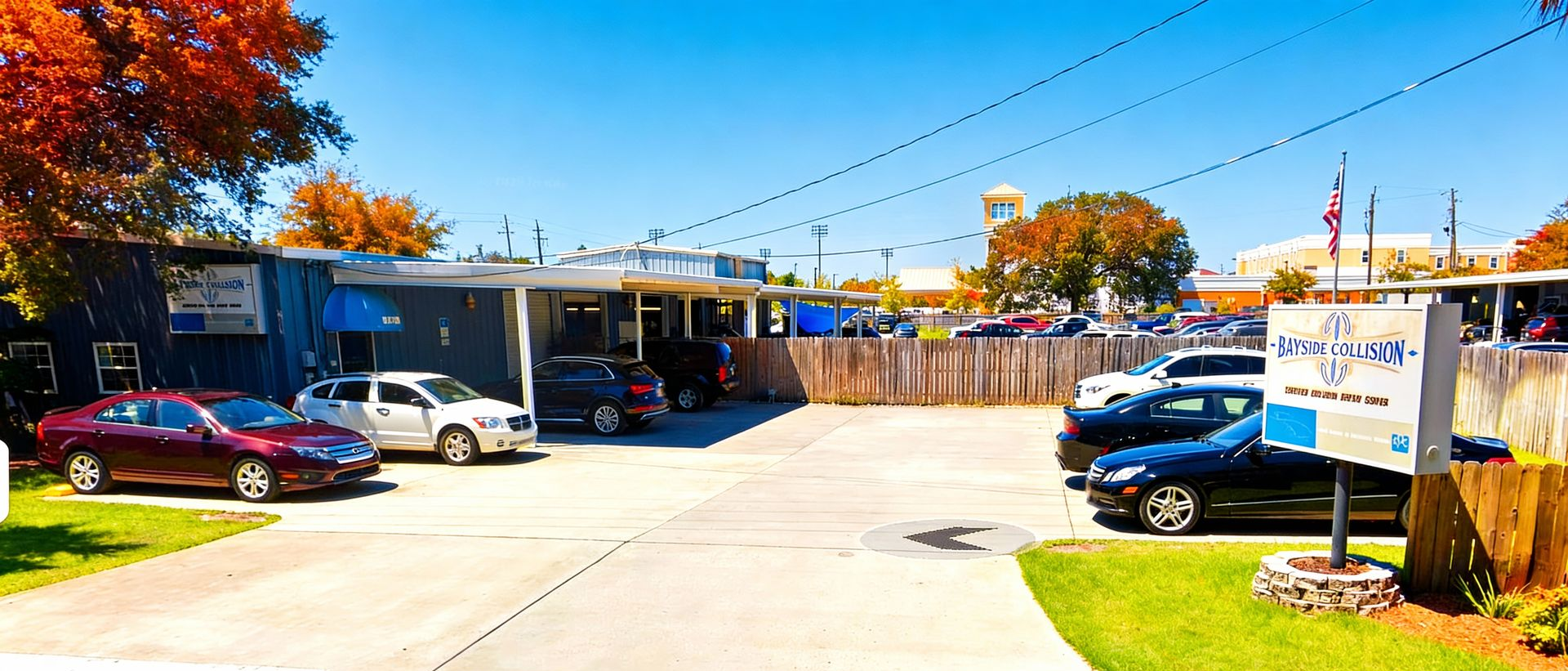 Exterior of a business with parked cars, a wooden fence, and a blue sky.