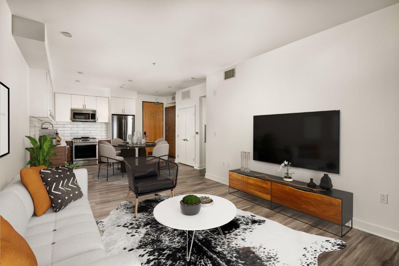 Modern living room with white walls, TV, sofa, and kitchen in background.