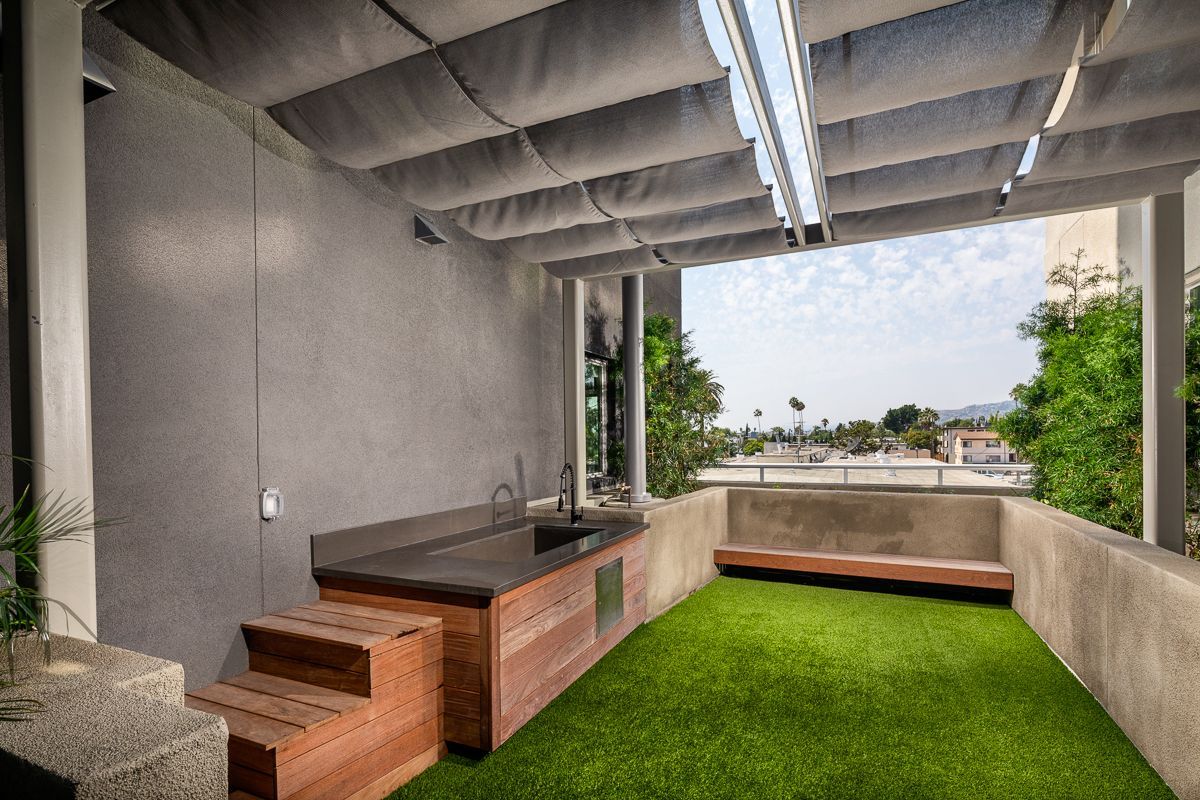 Outdoor patio with artificial turf, built-in counter and bench, shaded by a fabric awning, cityscape view.