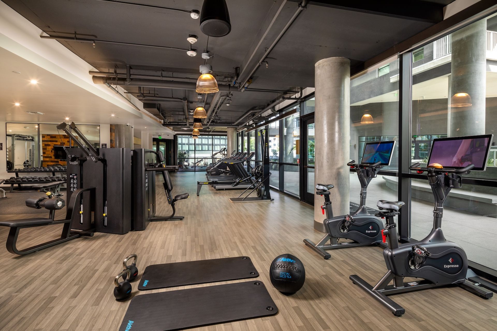 Gym interior with fitness equipment: treadmills, weights, stationary bikes, and mirrored wall.