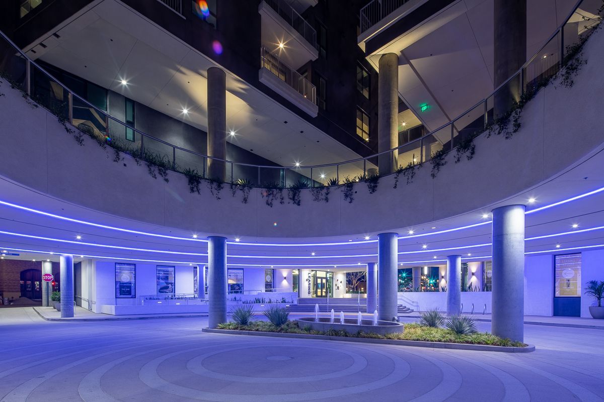 Night view of a modern building entrance with blue ambient lighting and a curved walkway.