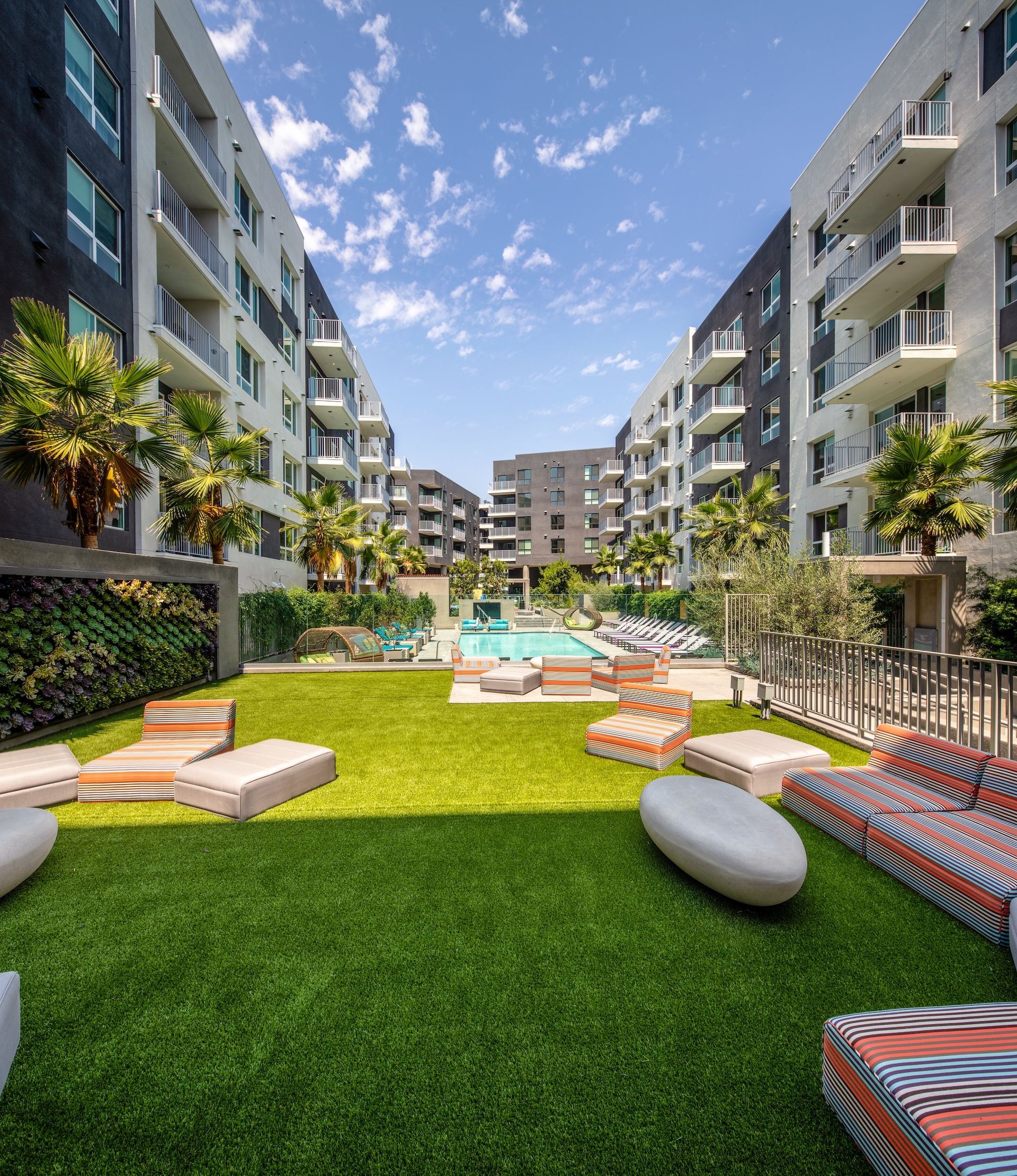 Apartment complex courtyard with a pool, lawn seating, and buildings on either side.