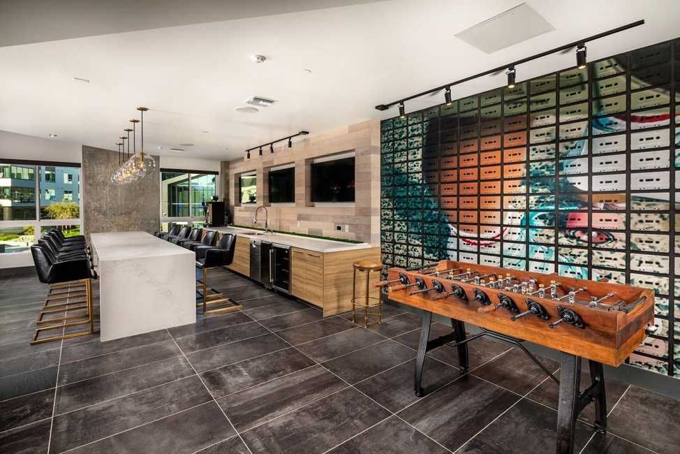 A clubroom bar with leather stools, quartz island, foosball table, and mosaic mural at The Ovelo Hollywood.