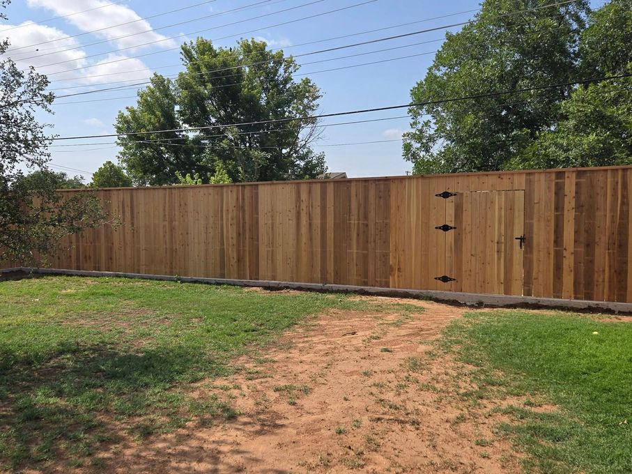 Wooden fence with a gate in a grassy yard under a blue sky.