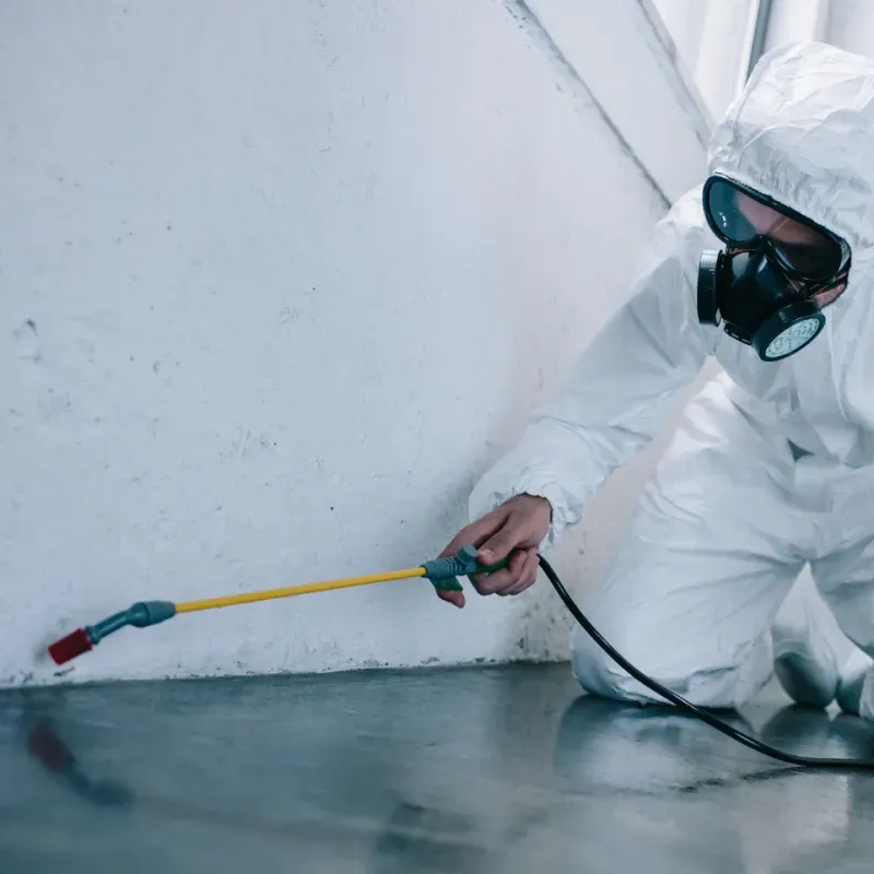 A man in a protective suit is spraying a wall with a sprayer.