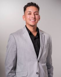 Smiling person in a light gray blazer and black shirt against a plain gray background