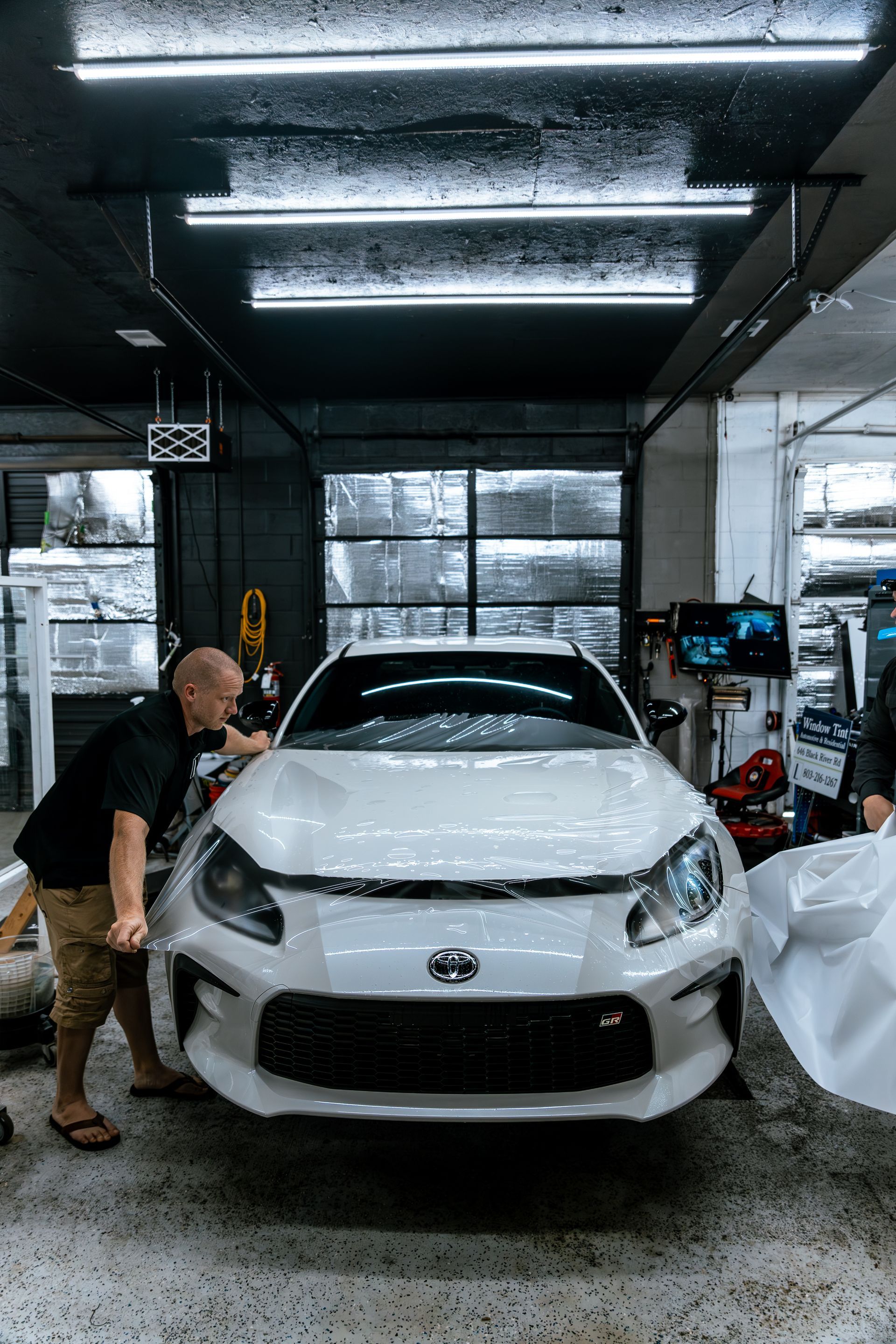 A man is wrapping a white car in a garage.