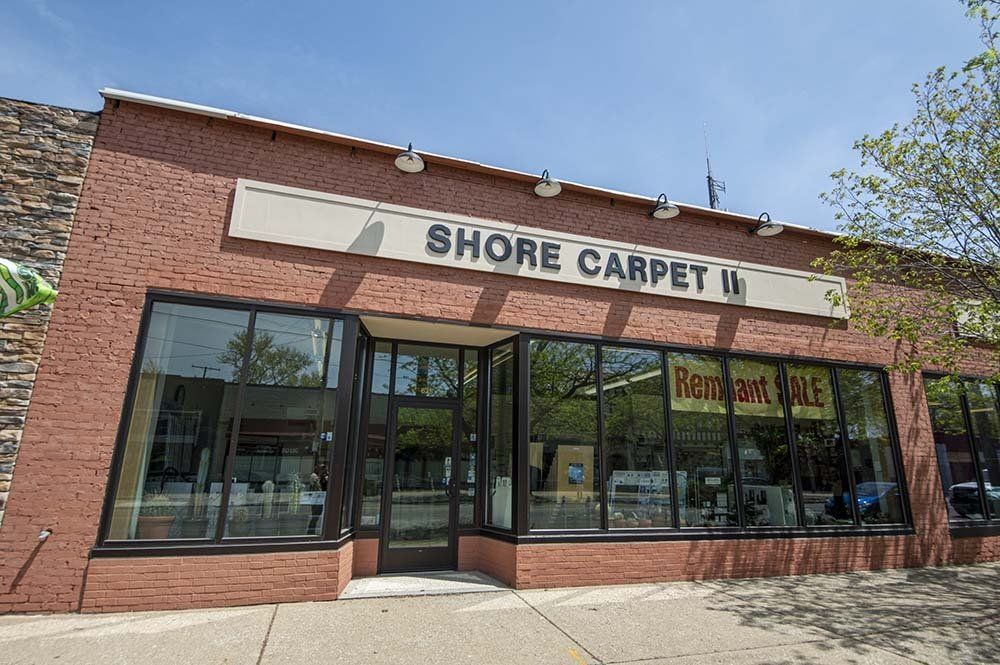 Shore Carpet store front in a brick building with large windows, signage, and sidewalk.